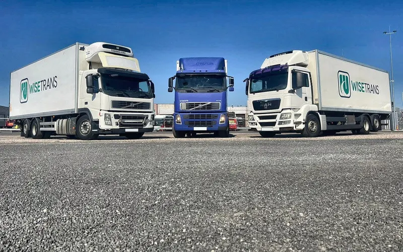 Three WiseTrans trucks in a car park under a blue sky